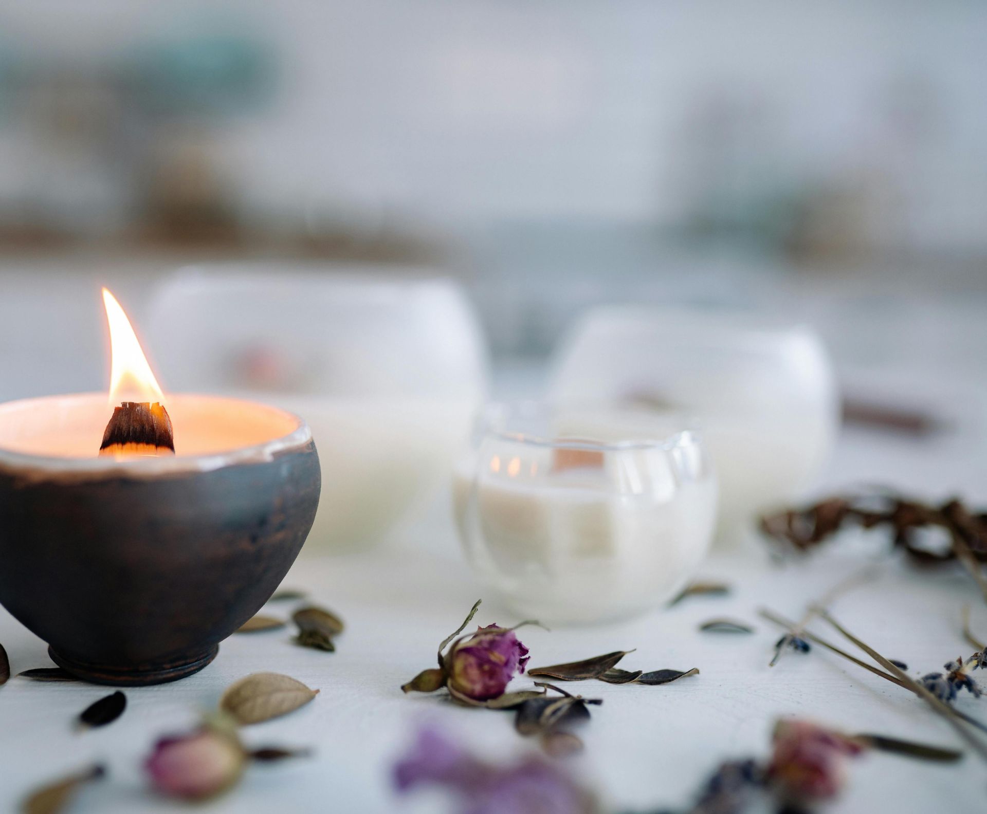 Warm candle flame in ceramic holder with dried flowers on table.