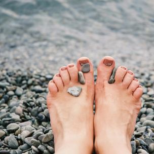 Close-up of female feet with stones on pebbled beach by the water, evoking relaxation and tranquility.