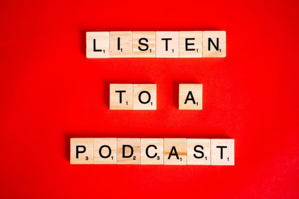 Scrabble tiles on red background forming the phrase 'Listen to a Podcast'.